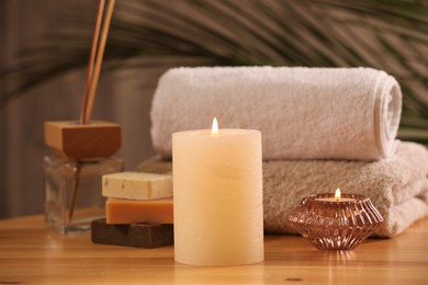 Photo of Spa composition. Burning candles, towels, soap and reed air freshener on wooden table, closeup