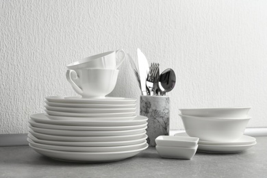 Photo of Set of clean dishes and cutlery on table near light wall