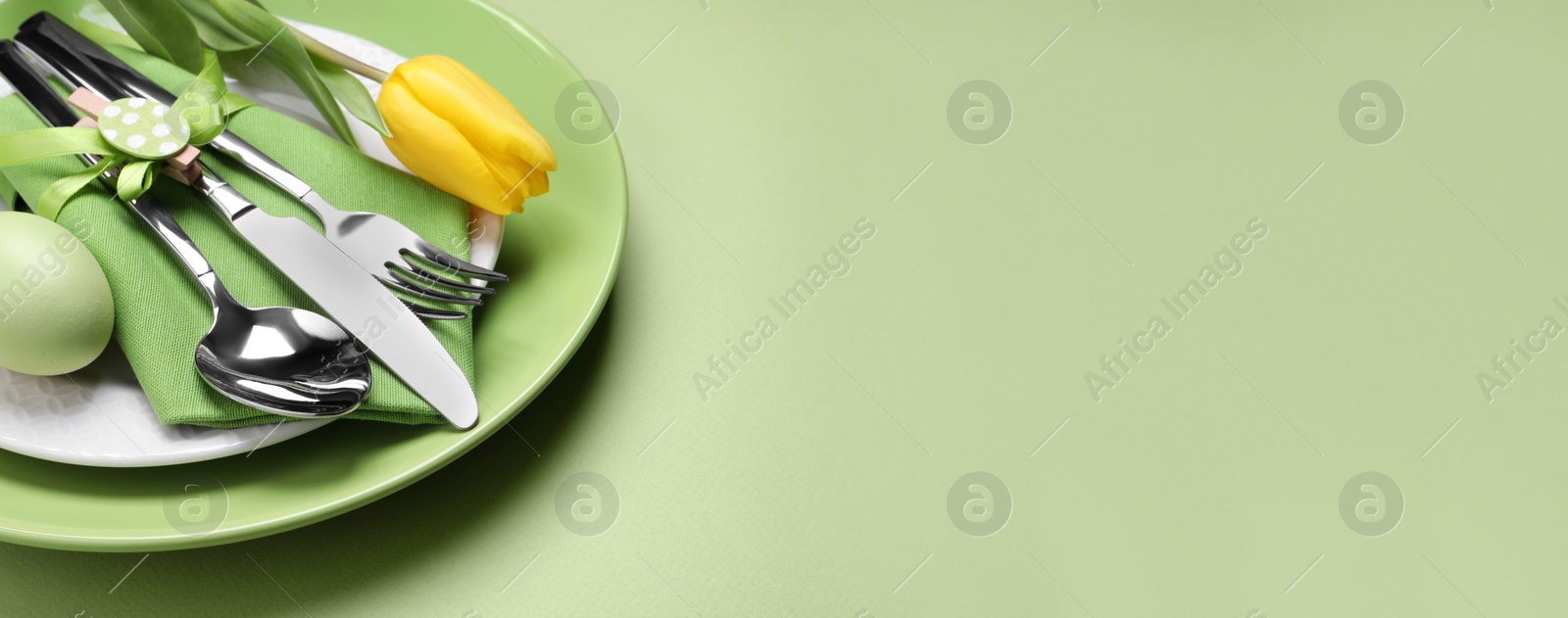 Photo of Festive Easter table setting with egg on light green background, closeup. Space for text