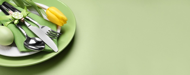 Festive Easter table setting with egg on light green background, closeup. Space for text