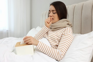 Photo of Sick young woman with box of tissues in bed at home