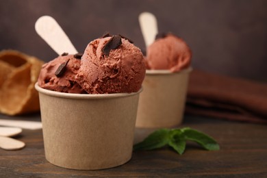 Photo of Paper cups with tasty chocolate ice cream on wooden table, closeup. Space for text