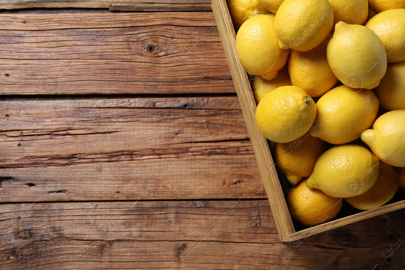 Photo of Fresh lemons in crate on wooden table, top view. Space for text