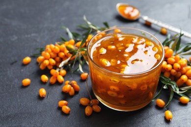 Photo of Delicious sea buckthorn jam and fresh berries on black table. Space for text