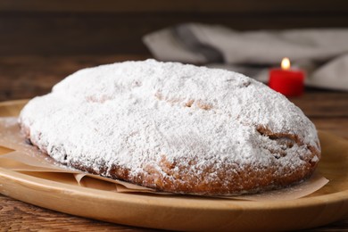 Photo of Wooden plate of delicious Stollen sprinkled with powdered sugar on table, closeup