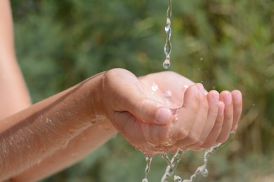 Photo of Pouring water into kid`s hands outdoors, closeup