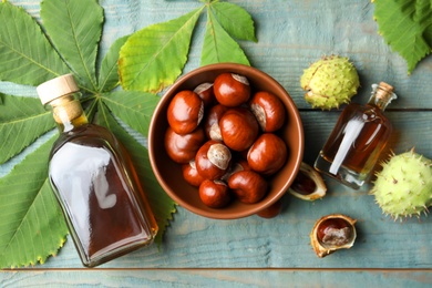 Photo of Chestnuts, leaves and bottles of essential oil on blue wooden table, flat lay