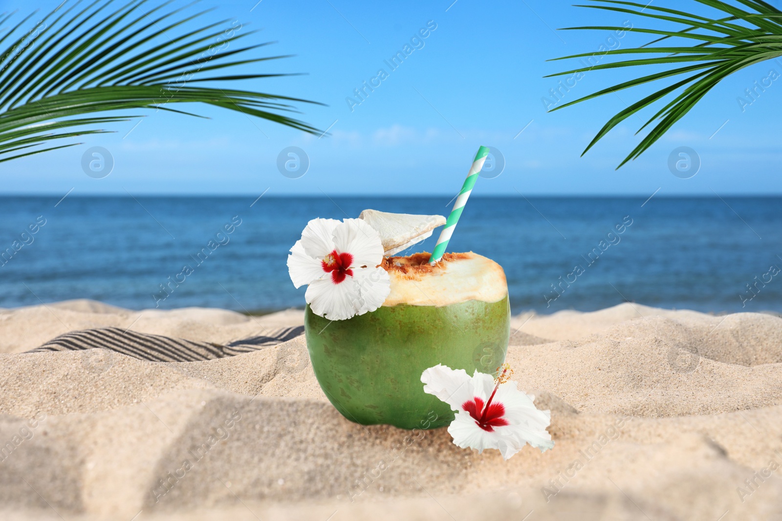 Image of Green coconut with refreshing drink and beautiful flowers on sandy beach near sea