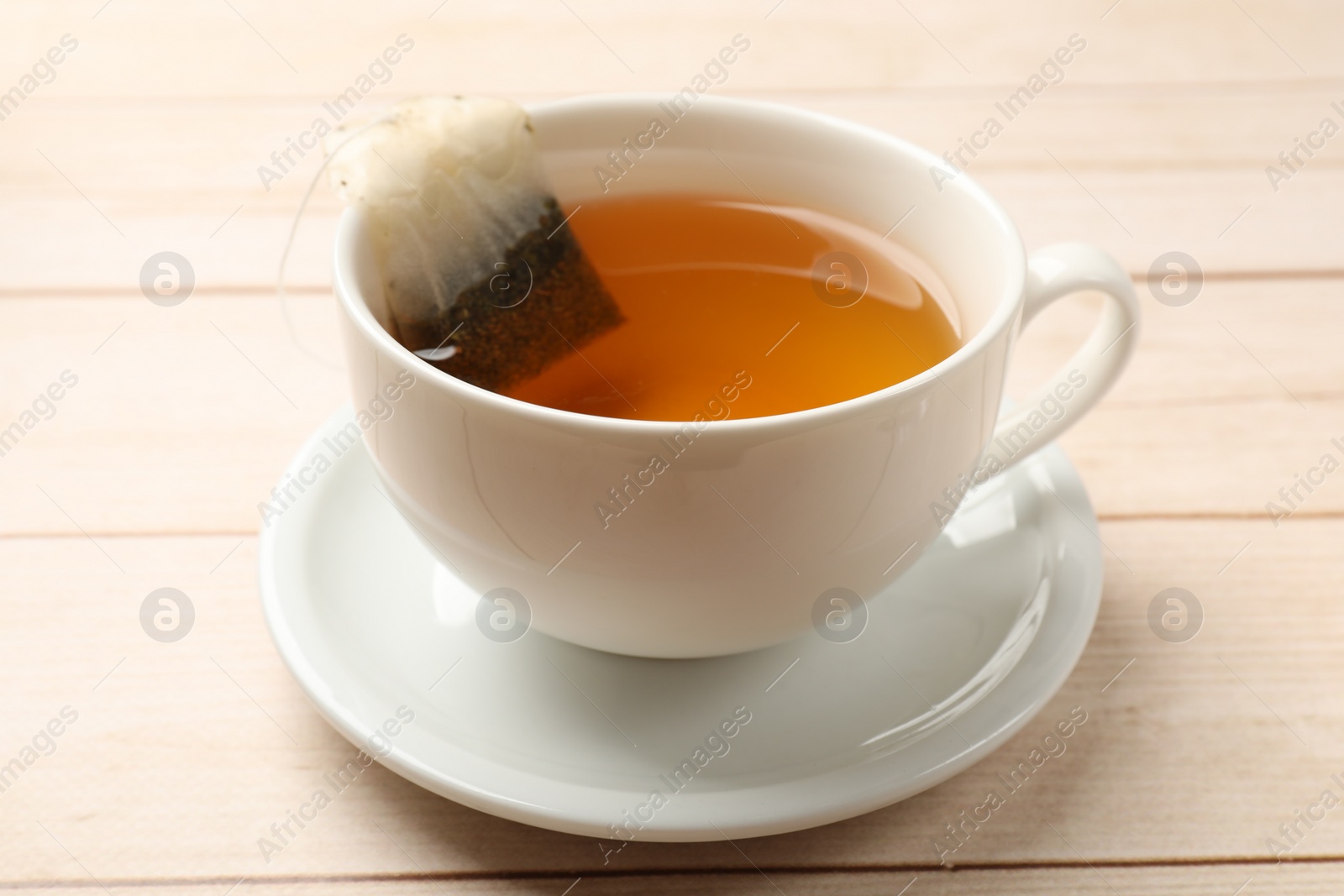 Photo of Tea bag in cup on light wooden table, closeup