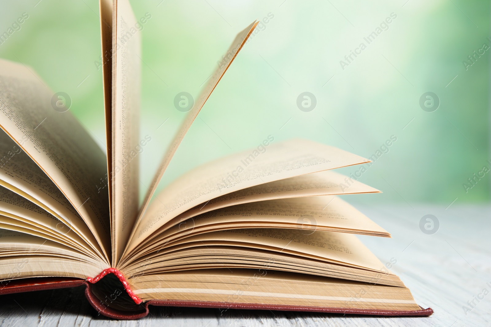 Photo of Open book on white wooden table against blurred green background, closeup