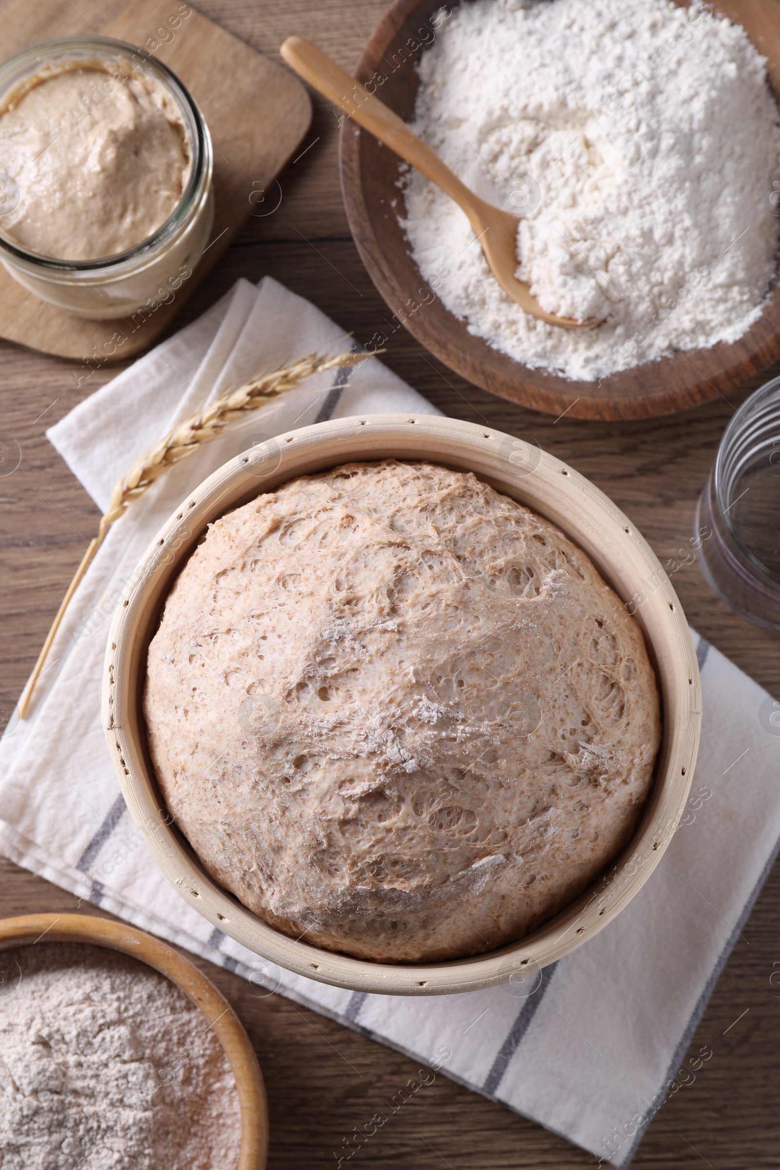 Photo of Fresh sourdough in proofing basket, flour and spike on wooden table, flat lay