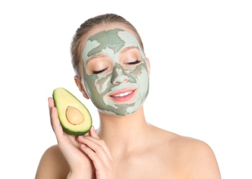 Beautiful woman holding avocado near her face with clay mask on white background