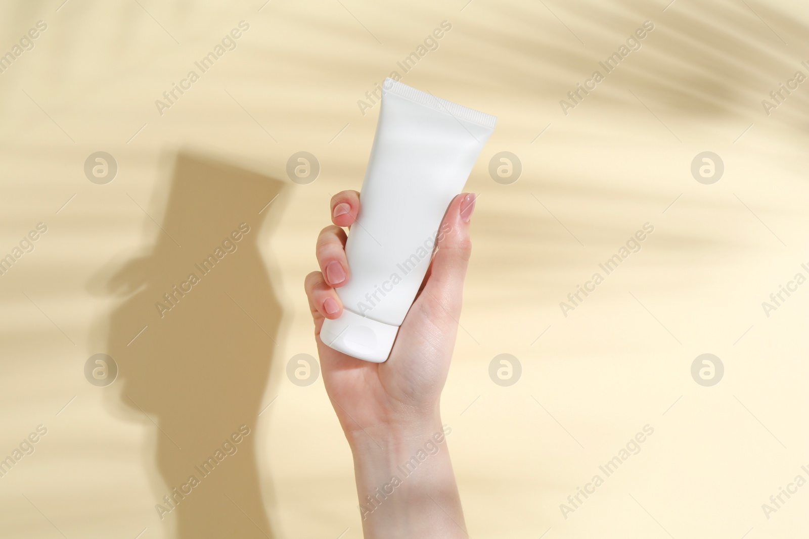 Photo of Woman holding tube of cream on yellow background, closeup