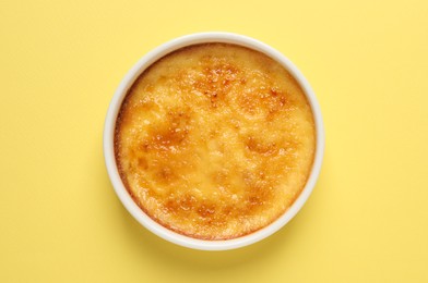 Photo of Delicious creme brulee in ceramic ramekin on yellow background, top view