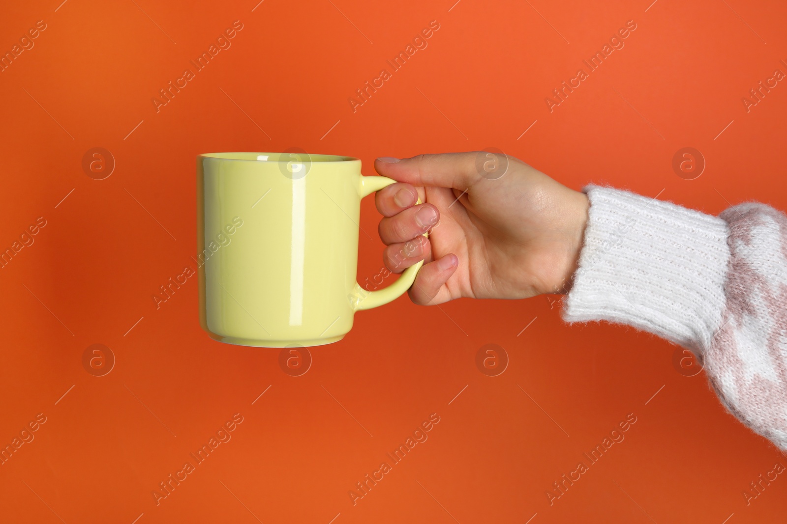 Photo of Woman holding yellow mug on orange background, closeup