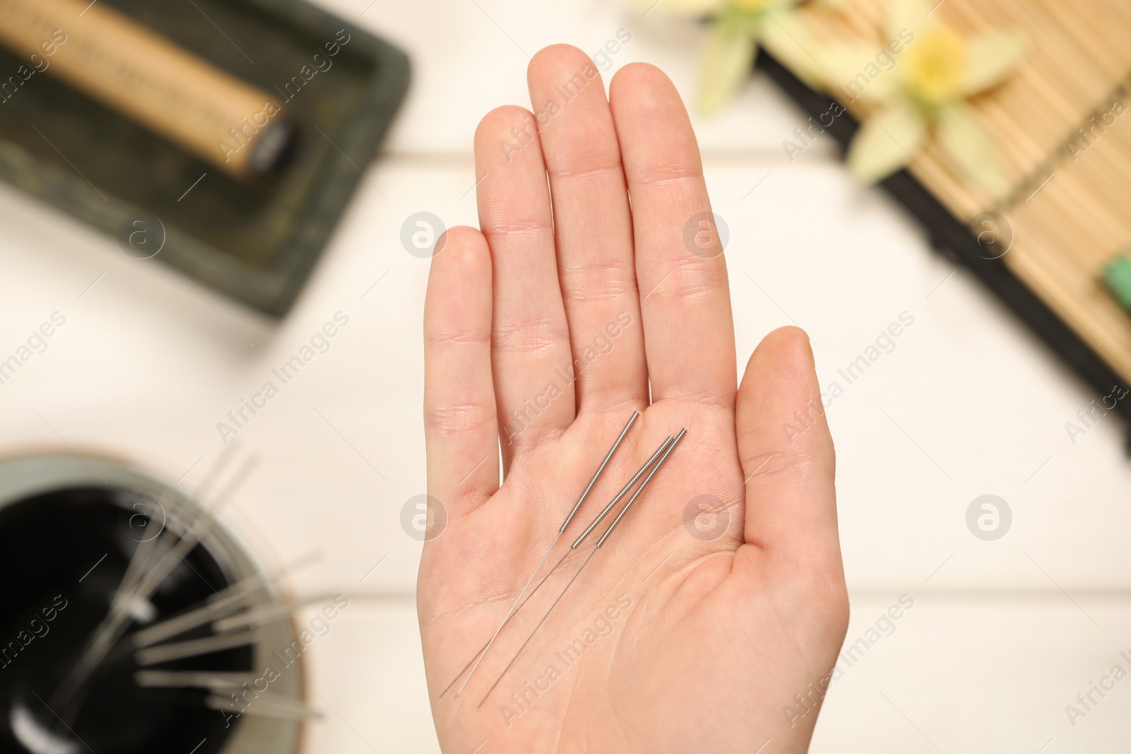 Photo of Woman holding many acupuncture needles over white wooden table, closeup