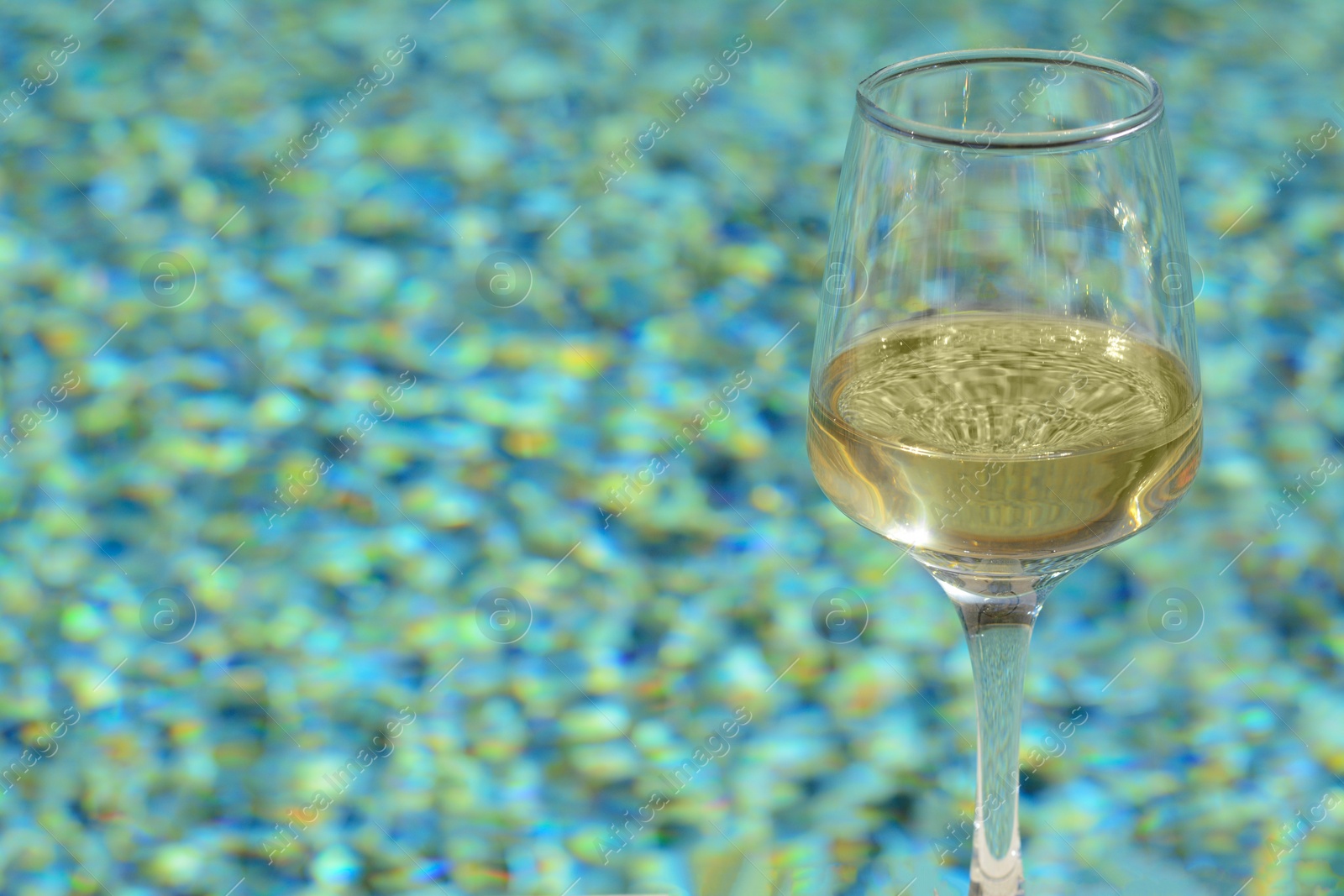 Photo of Glass of tasty wine near swimming pool, closeup. Space for text