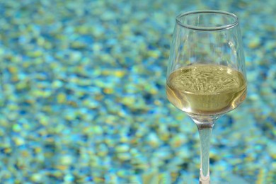 Photo of Glass of tasty wine near swimming pool, closeup. Space for text