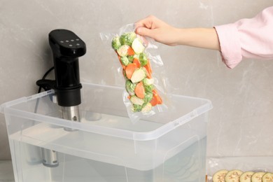 Photo of Woman putting vacuum packed vegetables into box with thermal immersion circulator, closeup. Sous vide cooking