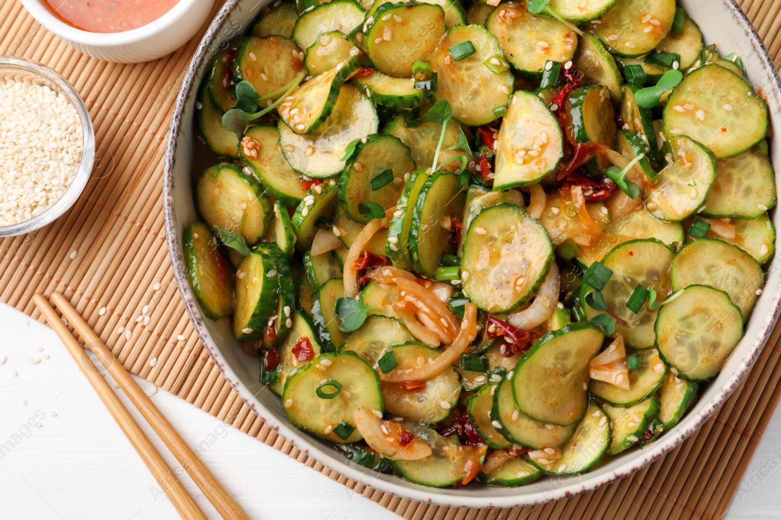 Photo of Bowl of delicious cucumber salad served on white wooden table, flat lay