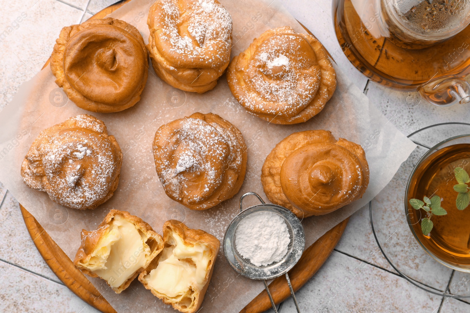 Photo of Delicious profiteroles filled with cream and tea on white tiled table, flat lay