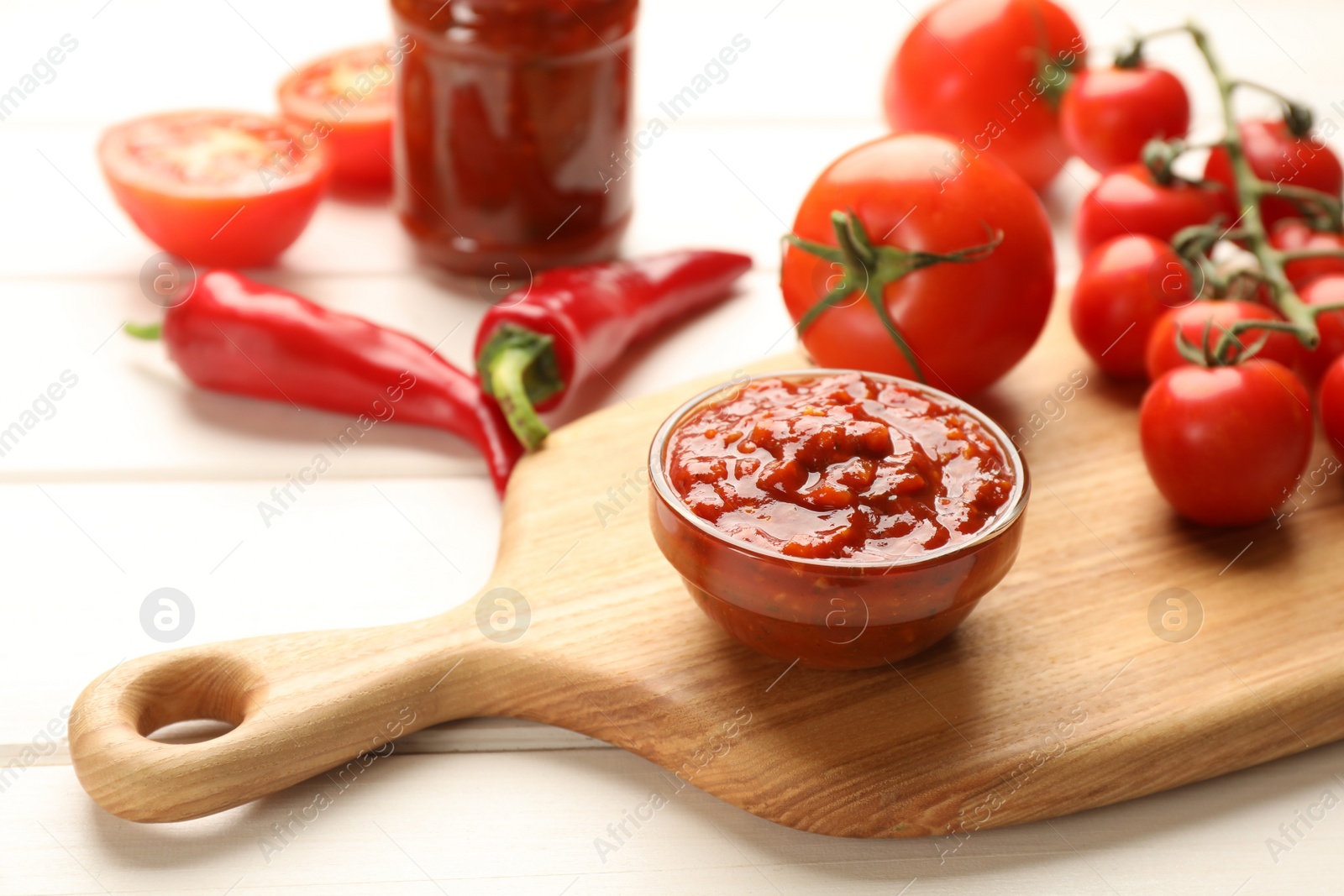 Photo of Delicious adjika sauce in bowl and ingredients on white wooden table