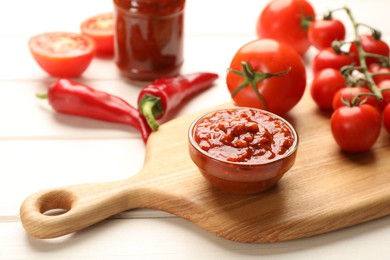 Delicious adjika sauce in bowl and ingredients on white wooden table