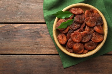 Bowl of tasty apricots and green leaves on wooden table, top view with space for text. Dried fruits