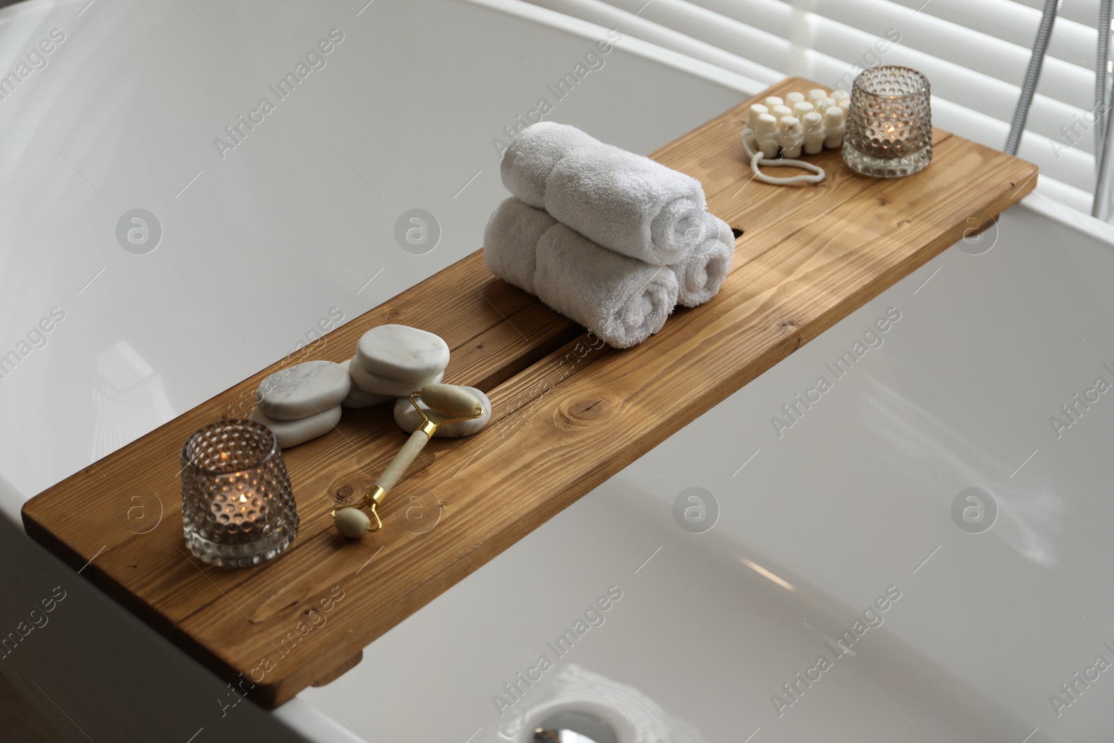 Photo of Wooden tray with spa products and burning candles on bath tub in bathroom