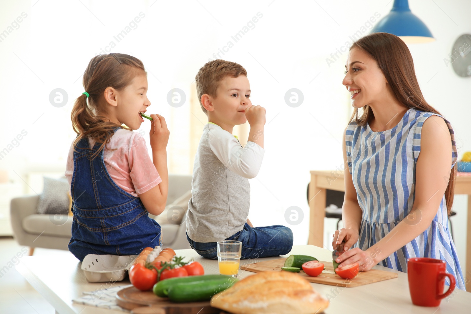 Photo of Young woman cooking breakfast for her children in kitchen. Happy family