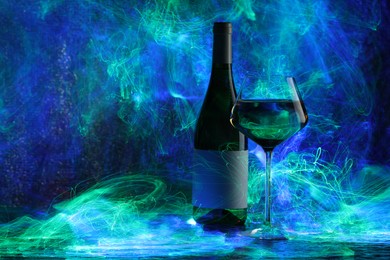 Photo of White wine in glass and bottle in color lights, space for text