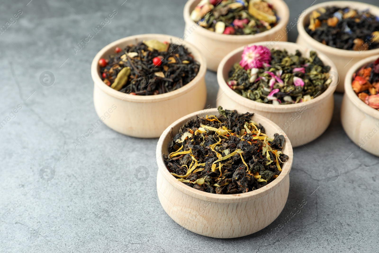 Photo of Different kinds of dry herbal tea in wooden bowls on light grey table. Space for text