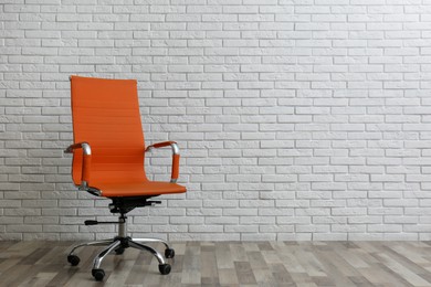 Comfortable office chair near white brick wall indoors. Space for text