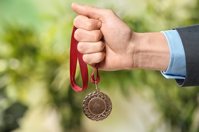 Photo of Man holding gold medal on blurred background, closeup