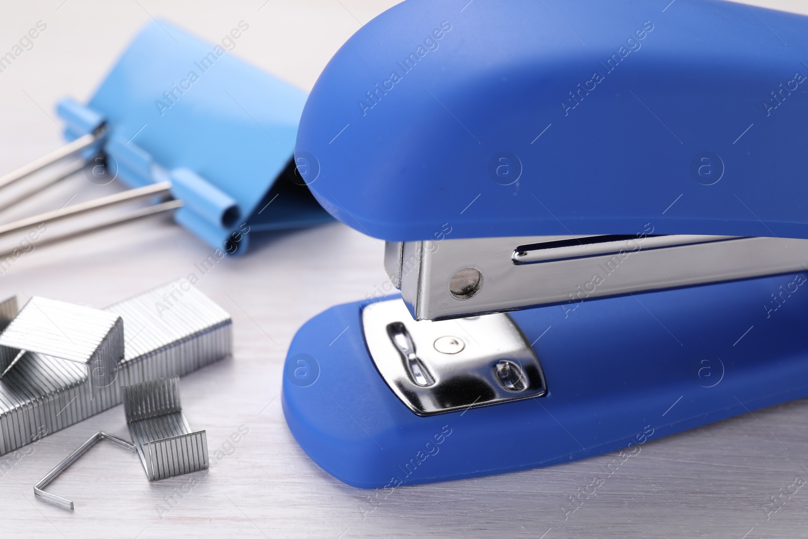 Photo of Blue stapler with staples on light wooden table, closeup