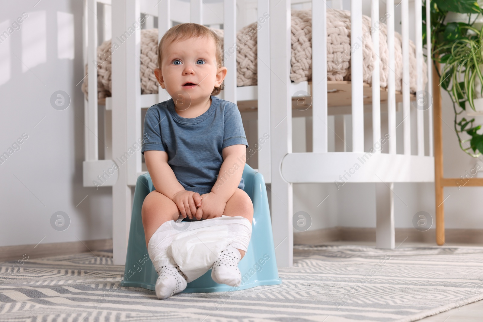 Photo of Little child sitting on plastic baby potty indoors. Space for text