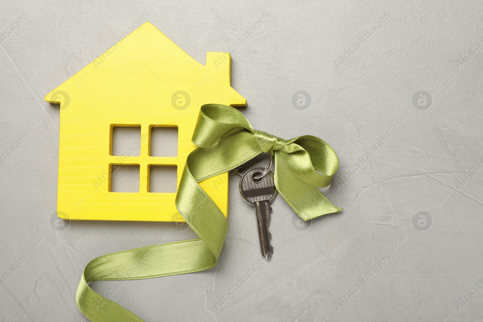 Photo of House model and key with bow on light grey stone background, flat lay. Housewarming party