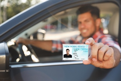 Photo of Happy man holding license while sitting in car outdoors, focus on hand. Driving school
