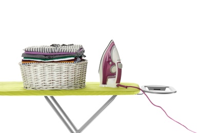 New modern iron and basket with clean laundry on board against white background