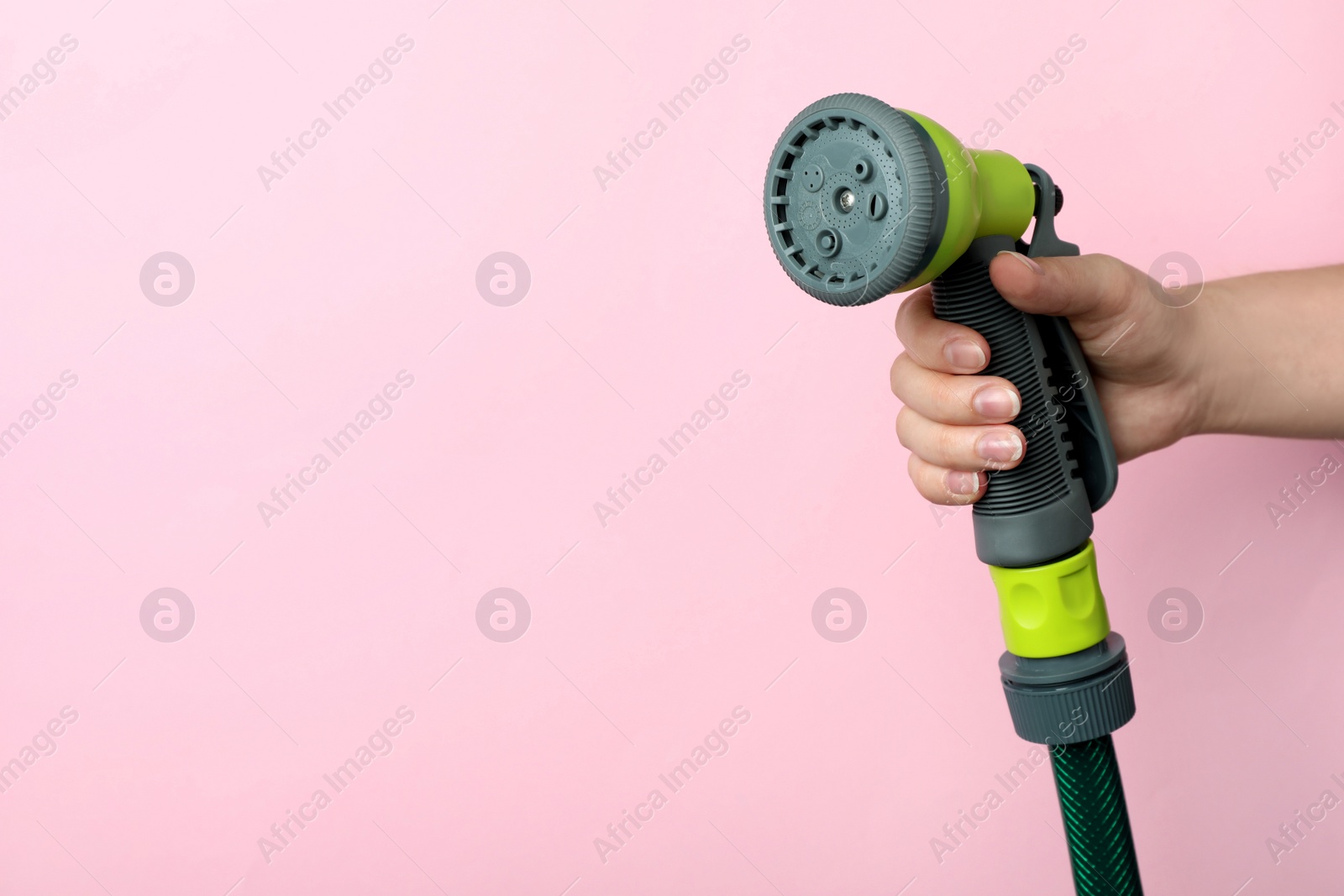 Photo of Woman holding watering hose with sprinkler on pink background, closeup. Space for text