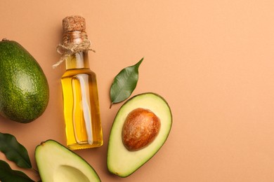 Photo of Glass bottle of cooking oil and fresh avocados on beige background, flat lay. Space for text