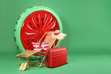 Deck chair, suitcase and beach accessories on green background, space for text