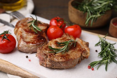 Delicious fried meat with rosemary and tomatoes on wooden board, closeup