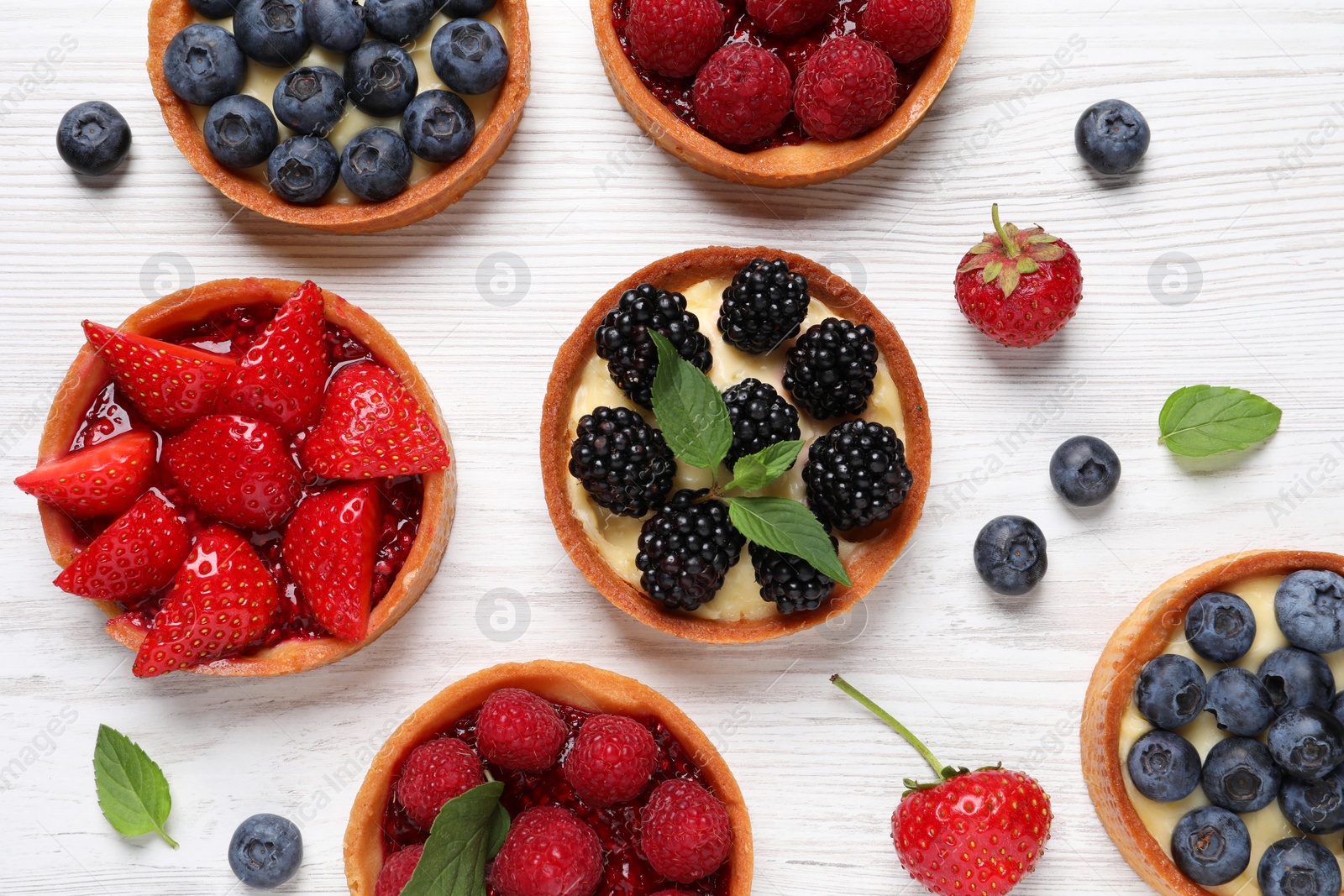 Photo of Tartlets with different fresh berries on white wooden table, flat lay. Delicious dessert