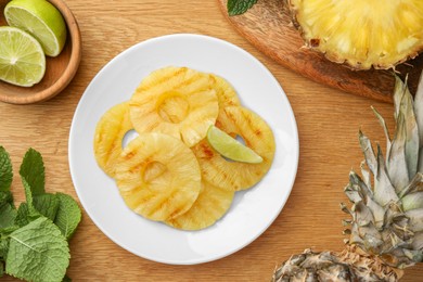 Photo of Tasty grilled pineapple slices, fresh lime and mint on wooden table, flat lay