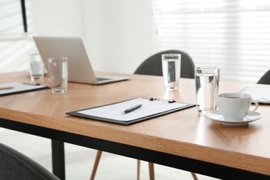 Photo of Conference room interior with glasses of water and clipboard on wooden table