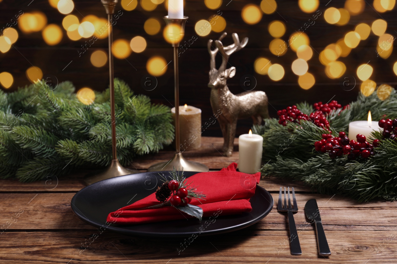 Photo of Plate with red fabric napkin, cutlery and festive decor on wooden table