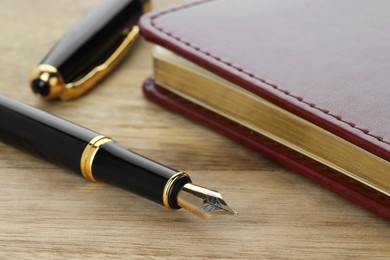 Photo of Stylish fountain pen, cap and notebook on wooden table, closeup