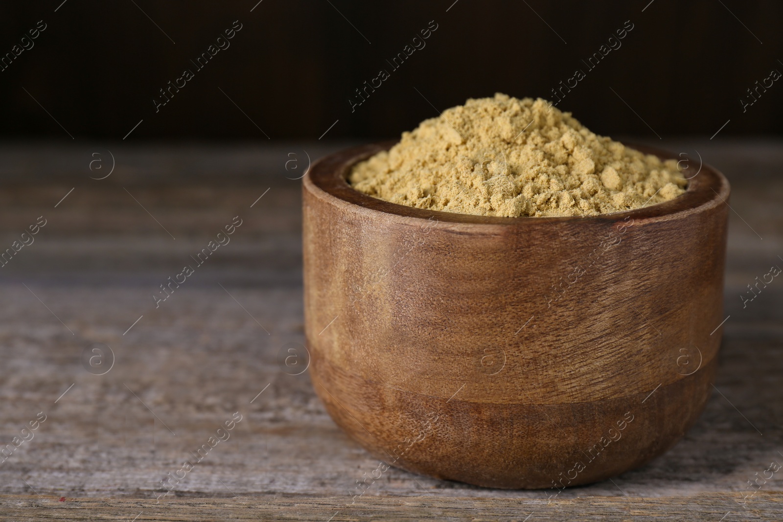 Photo of Bowl of mustard powder on wooden table, closeup. Space for text