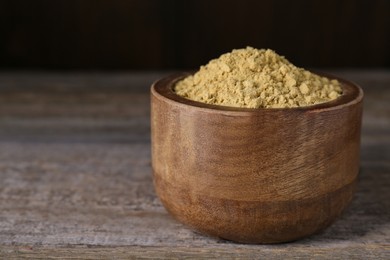 Photo of Bowl of mustard powder on wooden table, closeup. Space for text